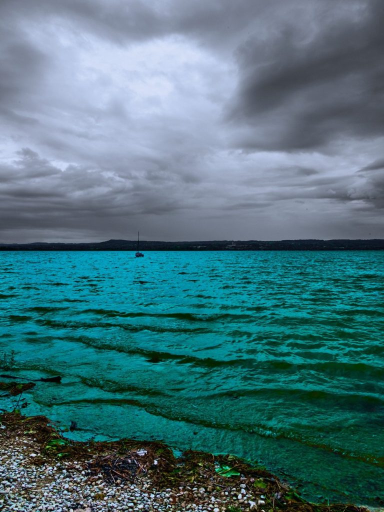 Klares Wasser mit sanften Wellen unter einem bewölkten Himmel.