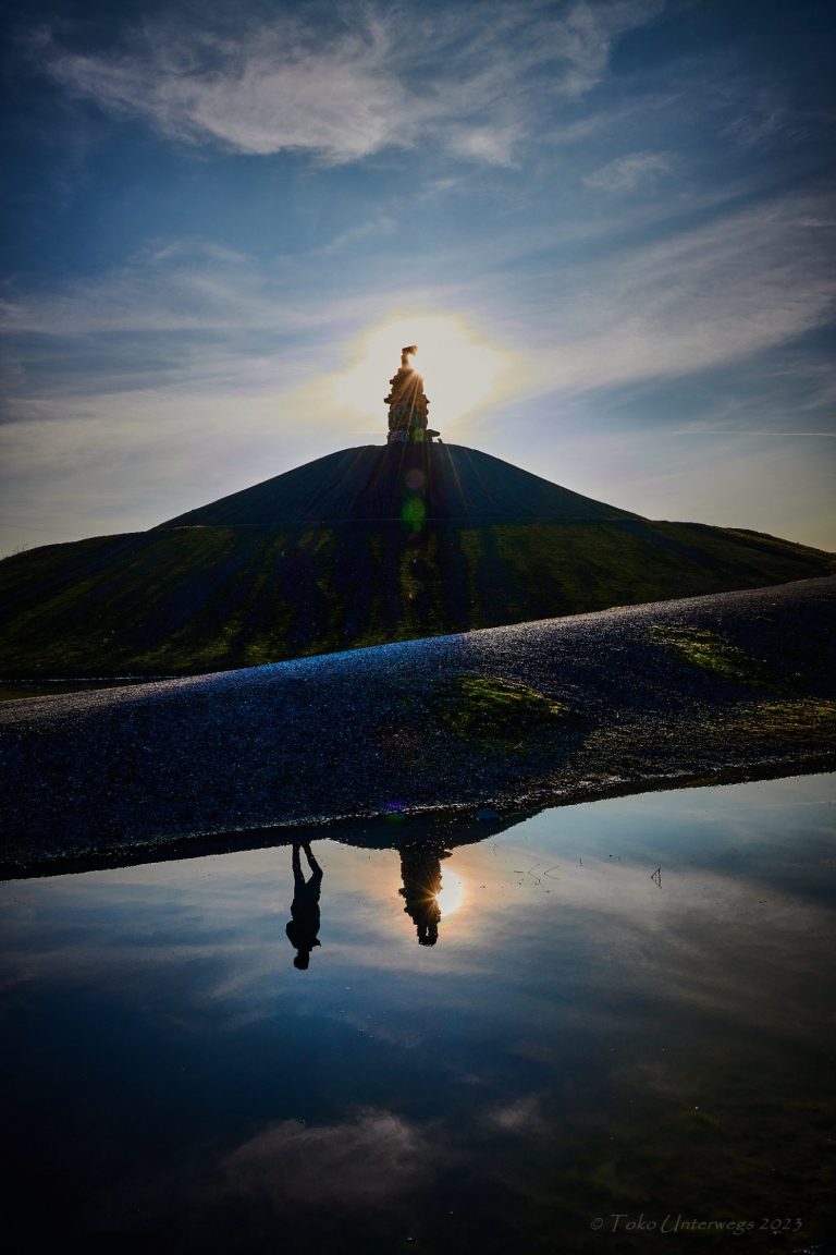 Blick auf eine Statue auf einem Hügel, reflektiert im Wasser bei Sonnenuntergang.